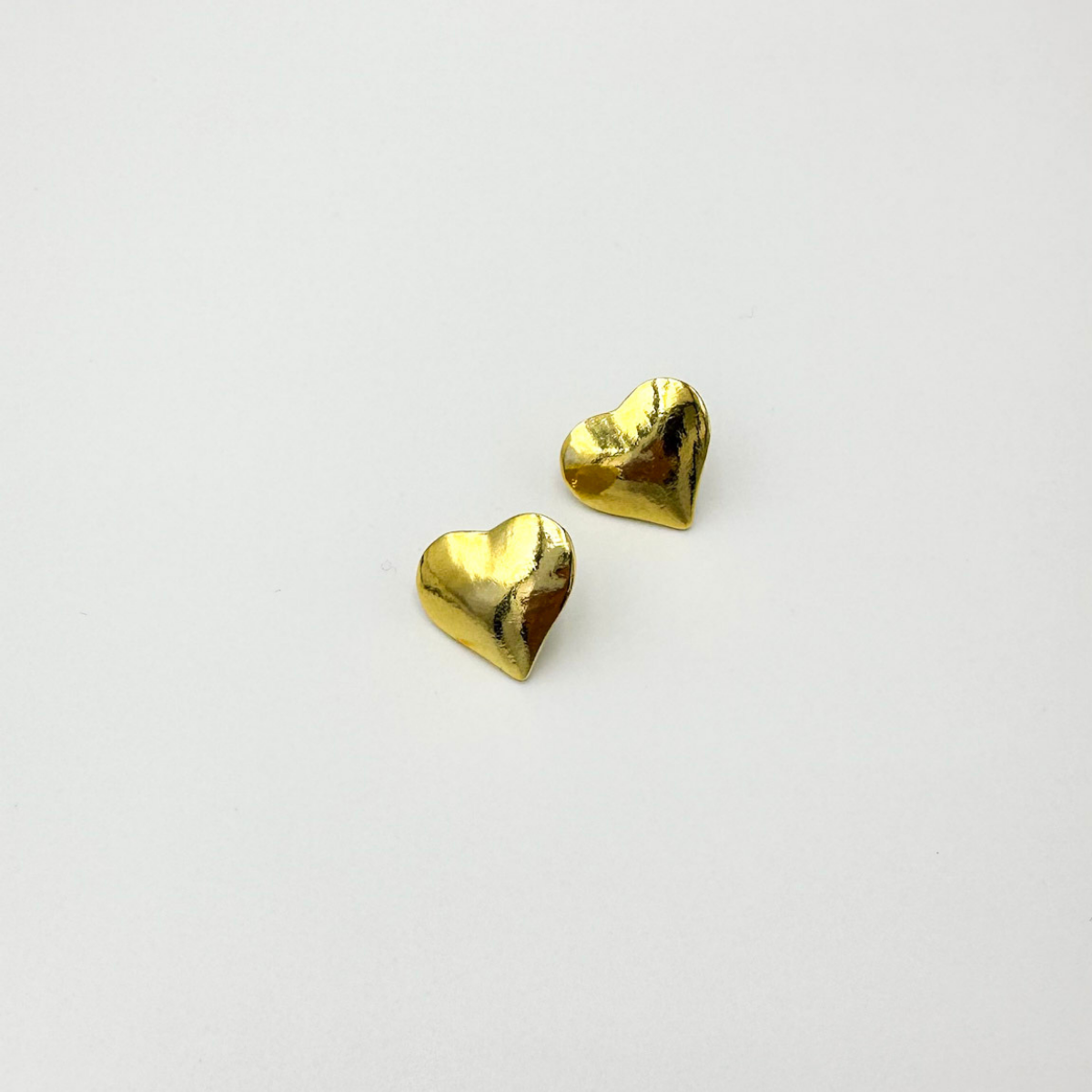 Aros Corazón Luisa dorados en forma de corazón con acabado brillante efecto espejo sobre fondo blanco