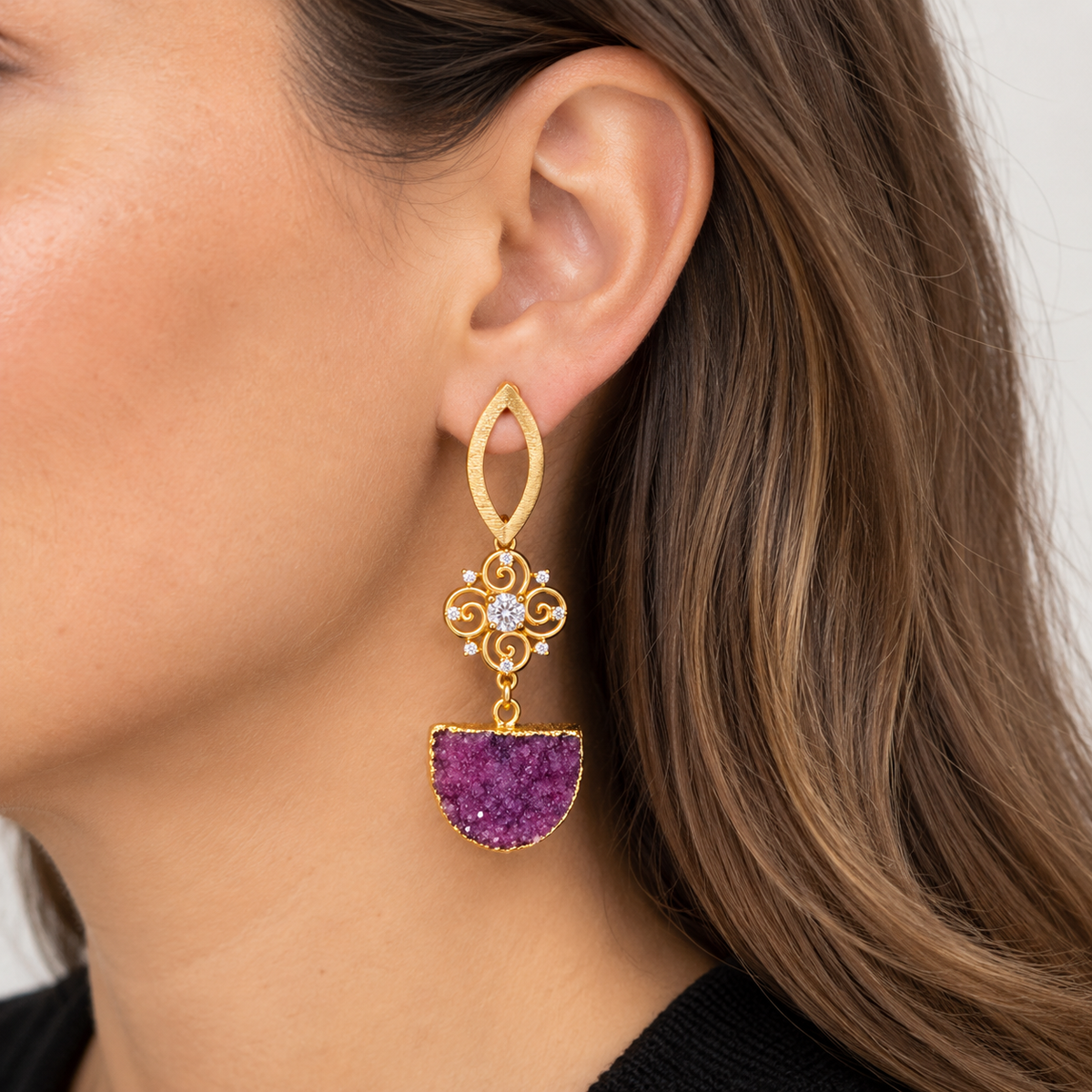 Aros dorados con piedra púrpura puestos en oreja de modelo MCJoyas