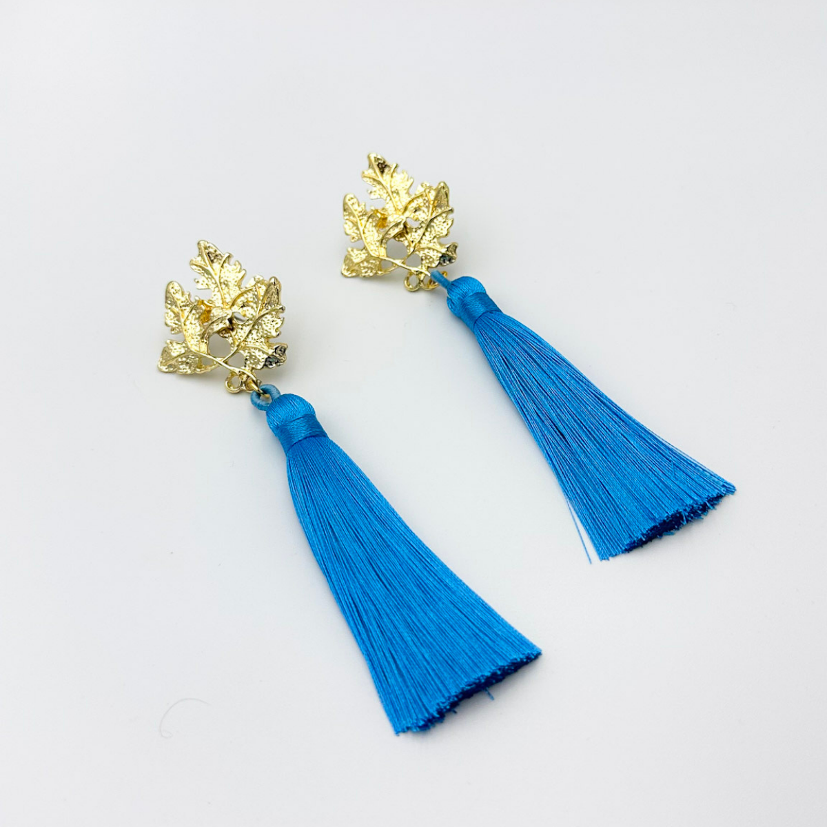 Aros largos con base de hojas doradas y borla azul intenso – MCJoyas.