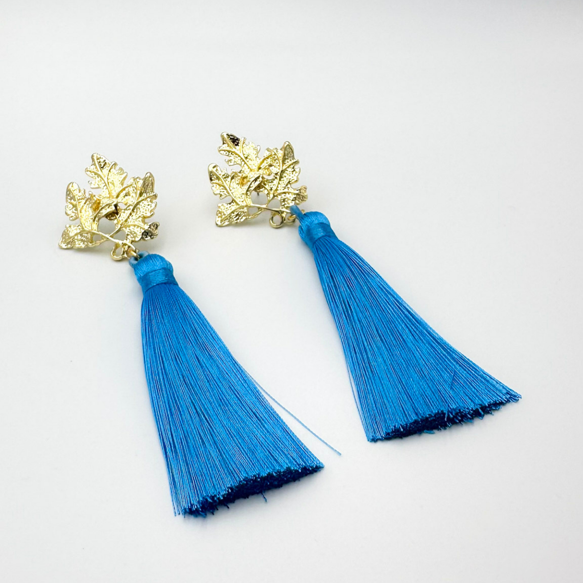 Aros largos con base de hojas doradas y borla azul intenso – MCJoyas