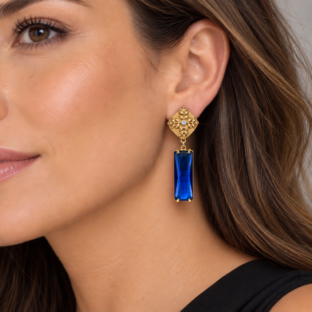 Mujer luciendo aros dorados con base floral y cristal azul facetado de MCJoyas