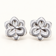 Par de aros clip en forma de flor plateada con pétalos en relieve y líneas grabadas, vista frontal