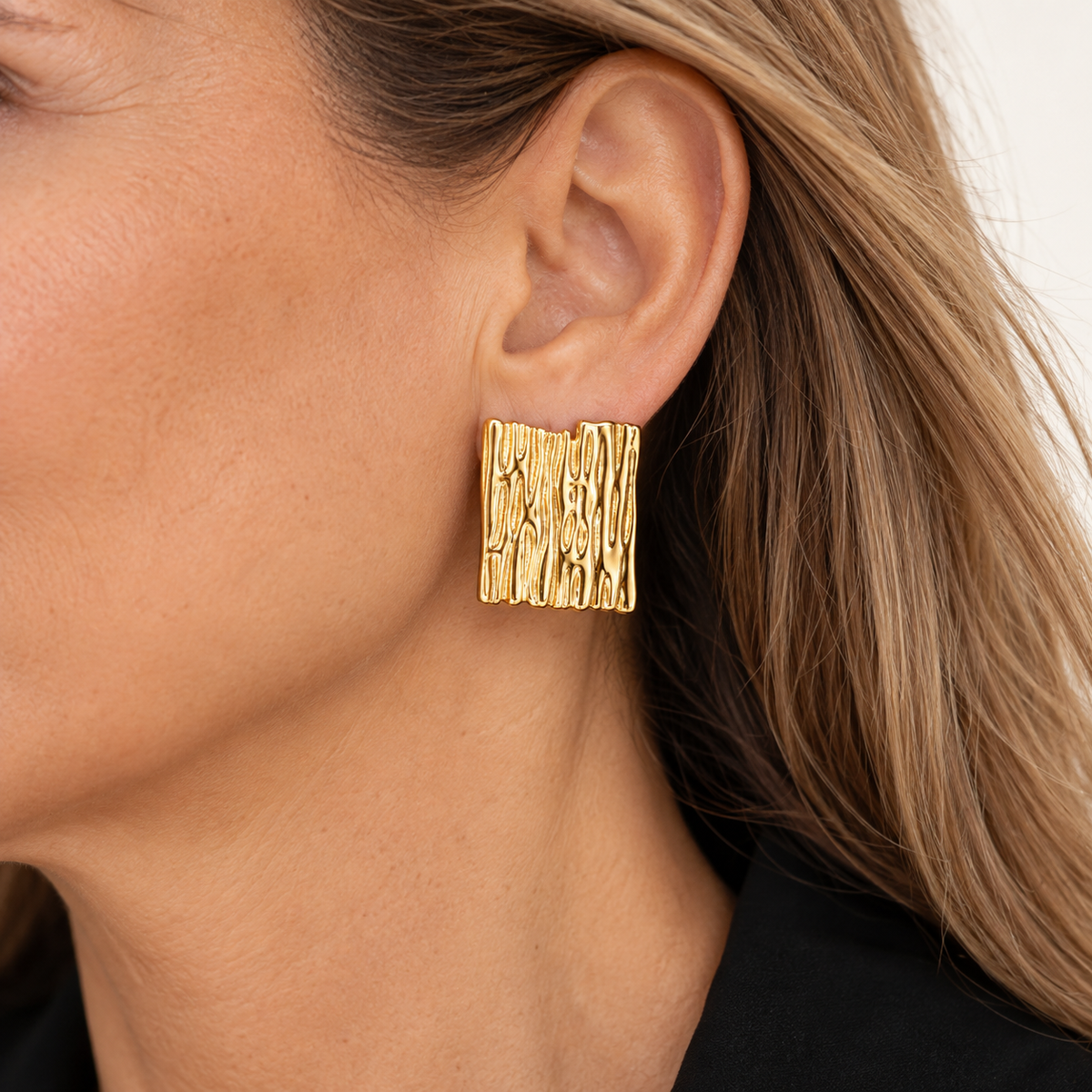 Par de aros clip rectangulares dorados con textura orgánica en relieve, puestos en una mujer